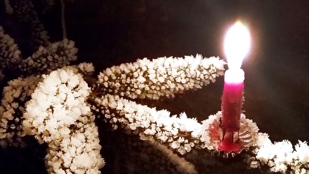 Brennende Kerze auf einem verschneiten Ast