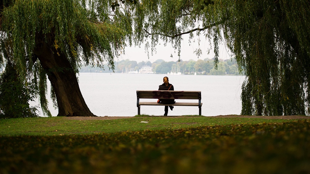 Ein Mann sitzt alleine auf einer Bank im Park