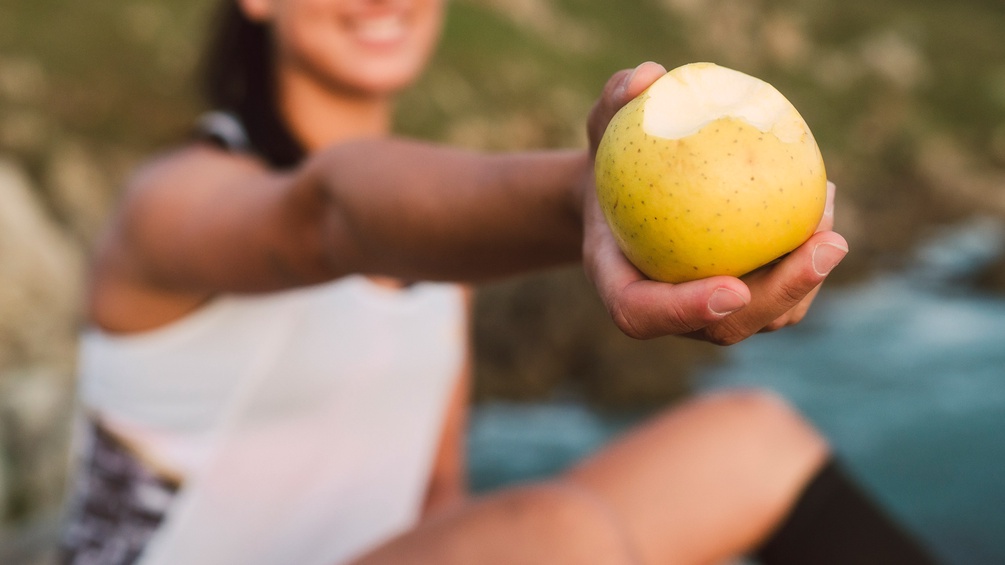 Frau reicht einen angebissenen Apfel