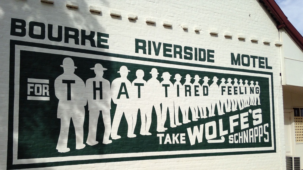 Hinweisschild an einer Hausmauer: Bourke Riverside Motel. "For that tired feeling take Wolfe's Schnapps."