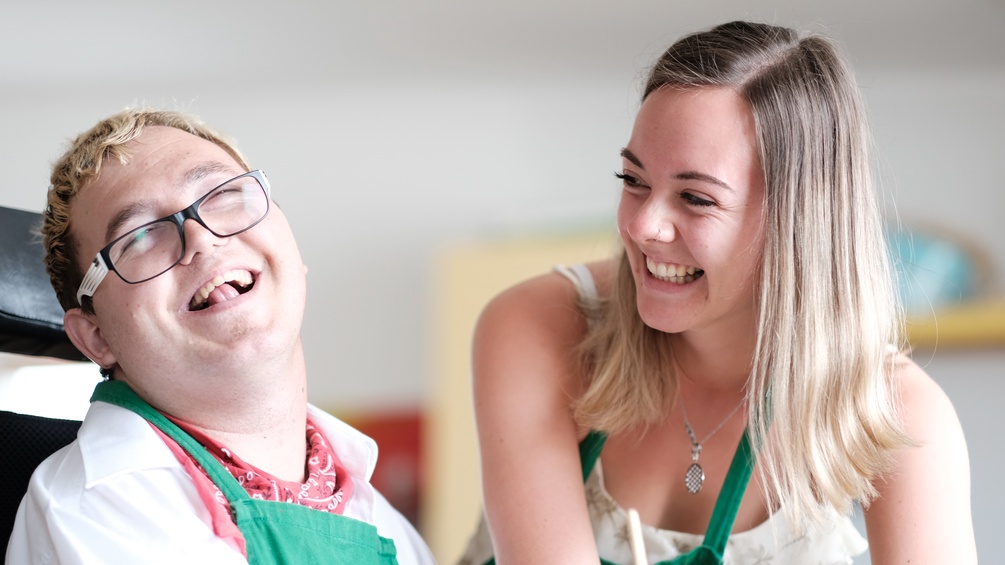 Eine junge Frau und ein Mensch mit Behinderung lachen