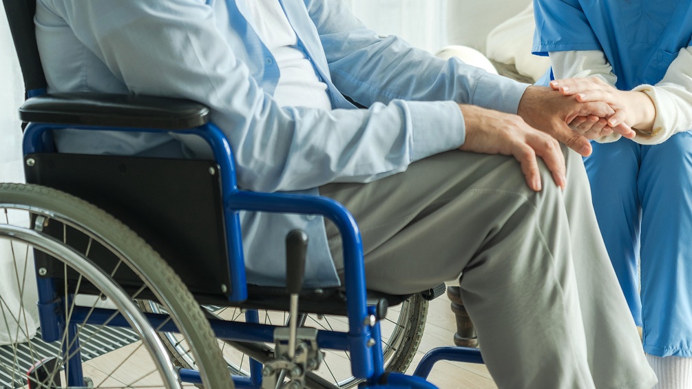Mann im Rollstuhl und Pflegepersonal, tröstende Hände