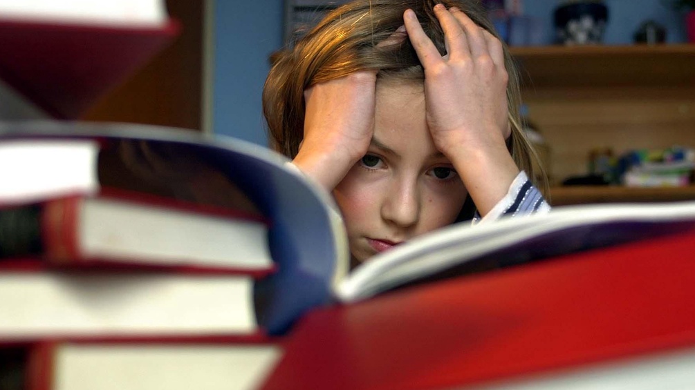 Ein Kind sitzt verzweifelt vor Schulbüchern.