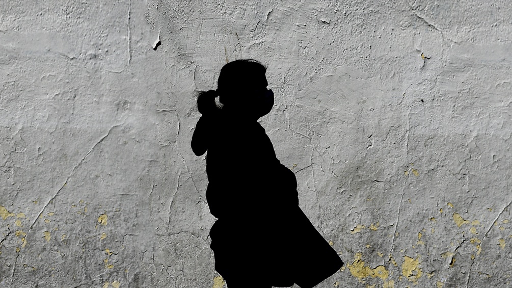 Der Schatten einer Frau mit Maske an einer Hauswand.
