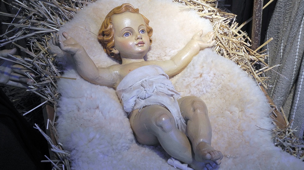 Ein Christkind aus Holz liegt in einem Strohbett.