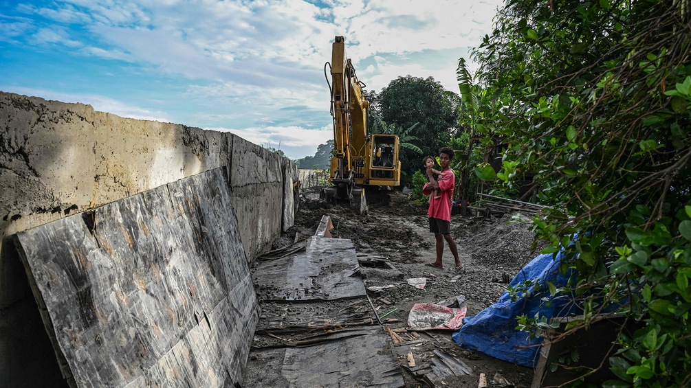 Ein Mann steht mit Kind in Armen neben einem unfertigen Damm in Plaridel in der Bulacan-Region, Philippinen