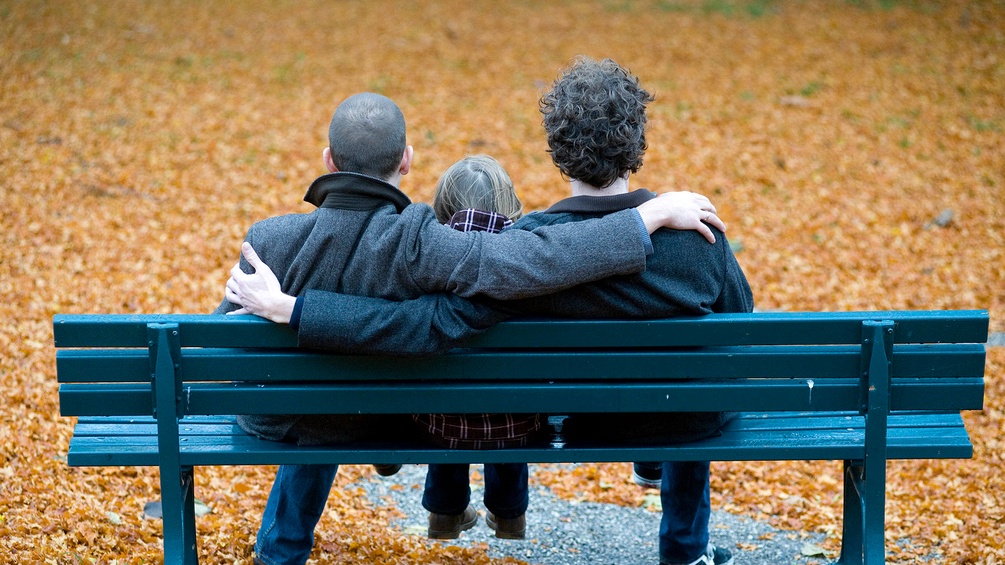 Homosexuelles Pärchen mit Kind auf einer Parkbank.