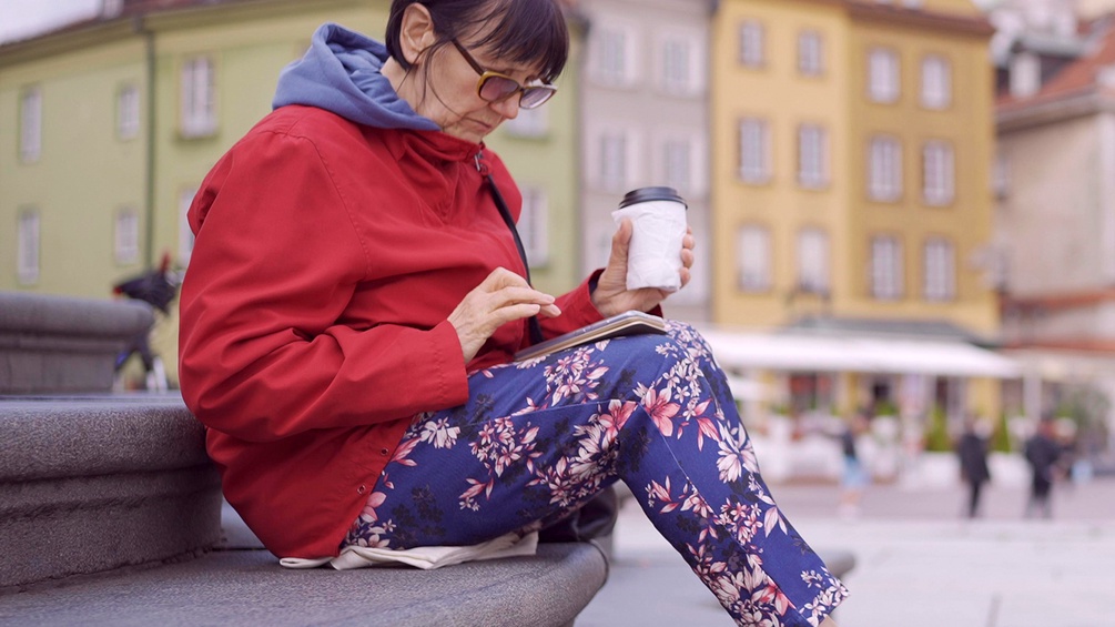 Frau sitzt an einem Brunnen mit einem Kaffee in der Hand und schaut auf ihre Smartphone