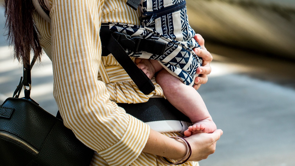 Frau trägt Baby in einer Trage
