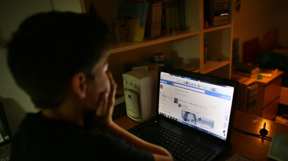 Kind sitzt vor dem Computer, Facebook ist geöffnet. Offenbar hat es etwas Schreckliches gesehen, denn es hält sich die Hände vors Gesicht.