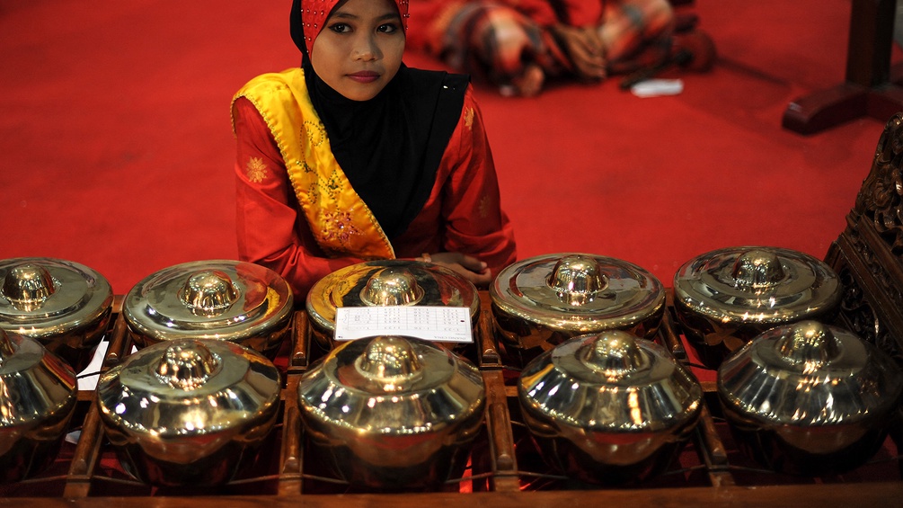 Eine Frau sitzt vor einer Reihe Gongs in Malaysien.