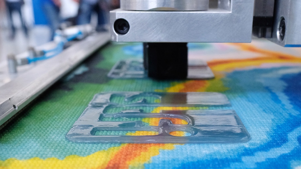 Textilforschung: 3D-Drucker produziert ein Logo auf einer textilen Fläche