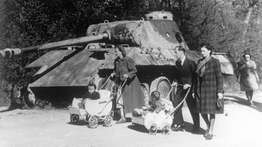 Der Fotograf inszeniert hier die Gleichzeitigkeit von Gewalt und Alltag 1945. Kinderwagen und Panzer sind aber auch Symbole für die Überwindung des Kriegs und den Neubeginn.