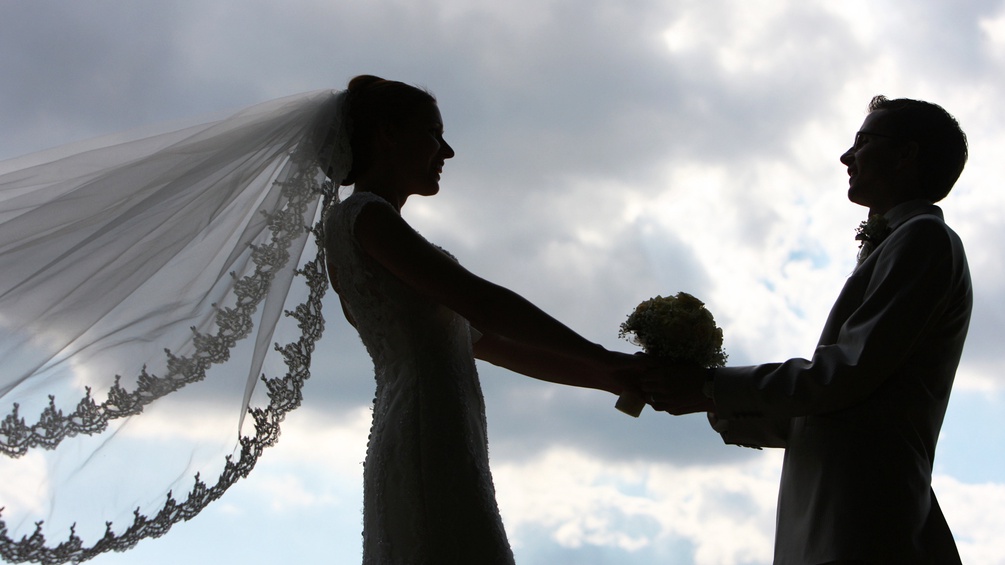 Silhouette eines Hochzeitspaares, der Schleier weht im Wind.