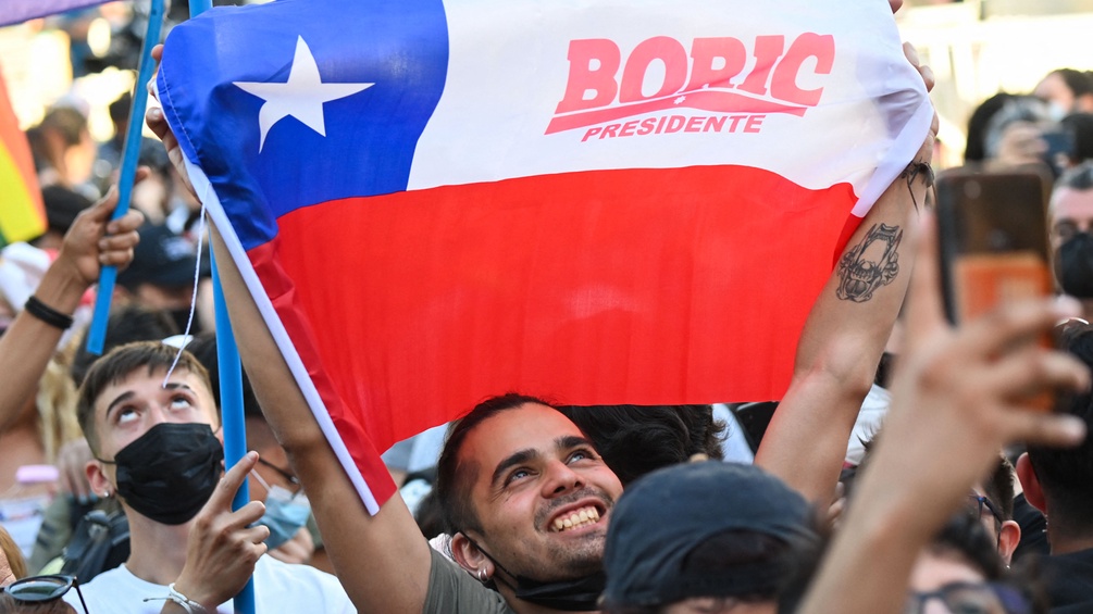 Ein Mann in einer Menschenmenge hält eine Boric Fahne in die Höhe.