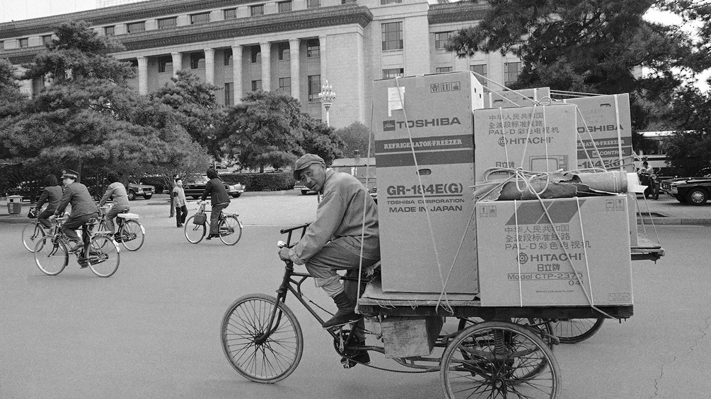 Mann in China auf dem Fahrrad mit westlichen Elektronikgeräten auf dem Anhänger