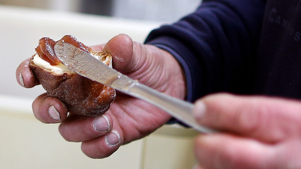 Obdachloser Mann bestreicht sich ein Stück Gebäck