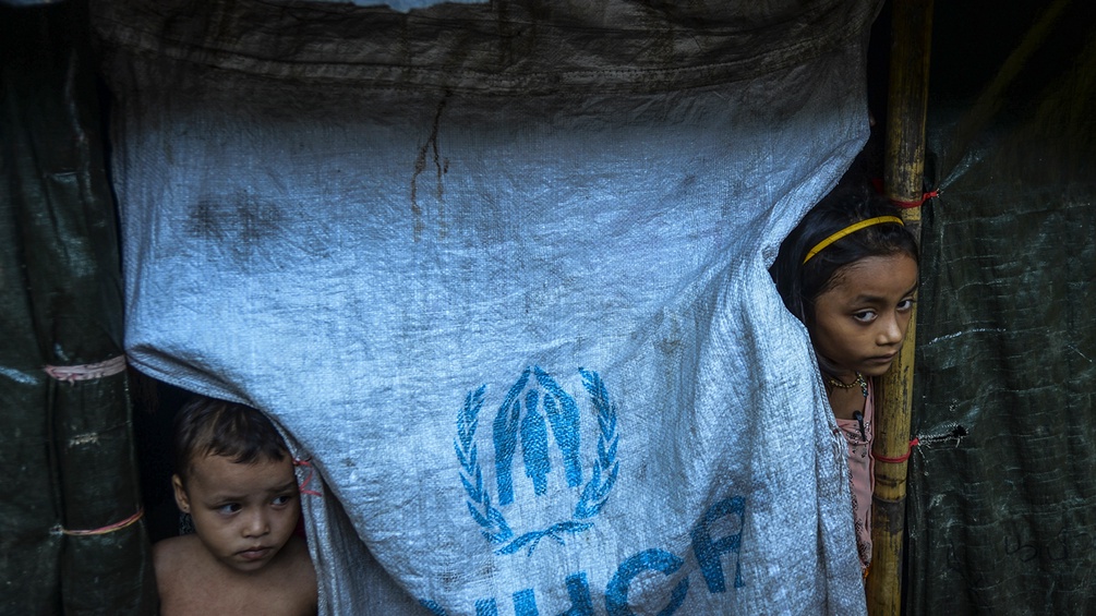 Zwei Kinder schauen unter einer Plane ihrer Flüchtlingsunterkunft hervor