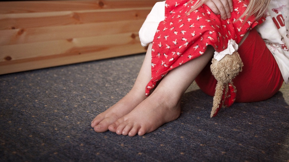 Kind hockt mit Stoffhasen auf dem Boden