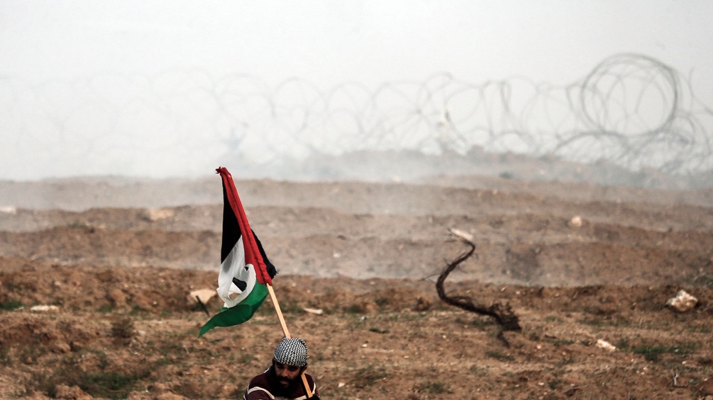 Ein Palästinenser hält eine Nationalflagge im Gaza-Streifen, dahinter Stacheldraht