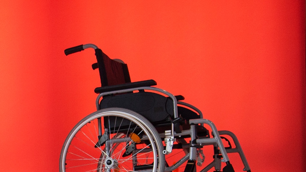 Ein Rollstuhl vor rotem Hintergrund.