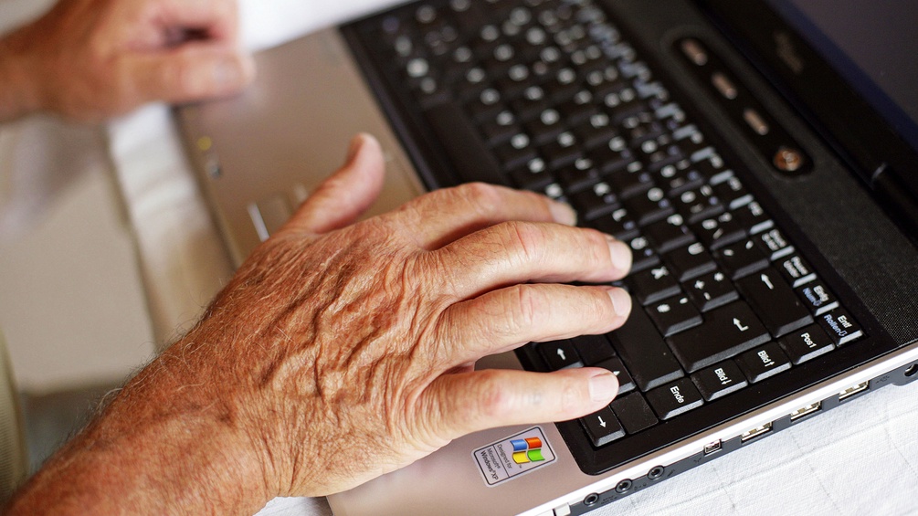 Die Hände eines alten Menschen schreibn auf einem Laptop