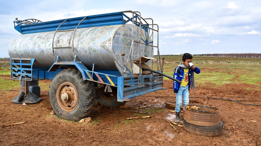 Kind trinkt Wasser von einem Wassertank in einem Camp