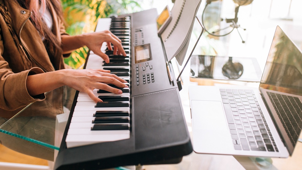 Frau nimmt zuhause am Keyboard Musik auf, Laptop