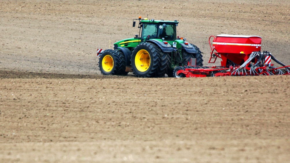 Ein Traktor fährt über einen Acker und bringt Saatgut und Dünger aus. 