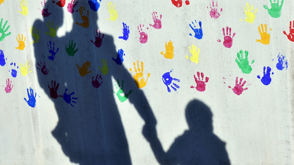 Schatten eines Erwachsenen mit Kindern, bunte Handflächen auf der Betonwand.