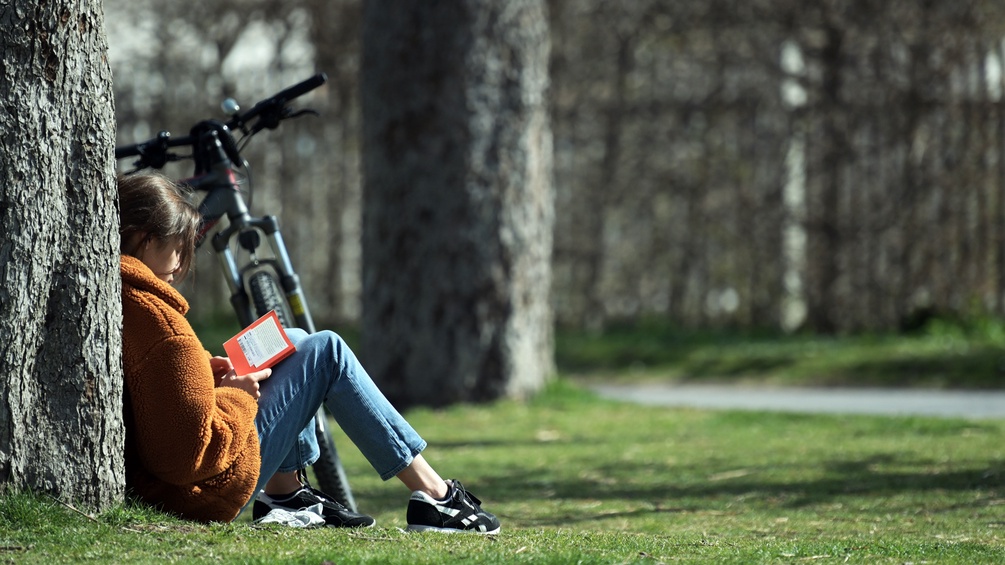 Eine Frau sitzt in einem Park am Boden und liest.Sie hat ihr Rad dabei.