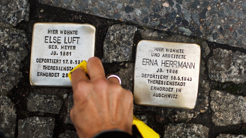 Eine Frau putzt Erinnerungssteine von deportierten jüdischen Opfern