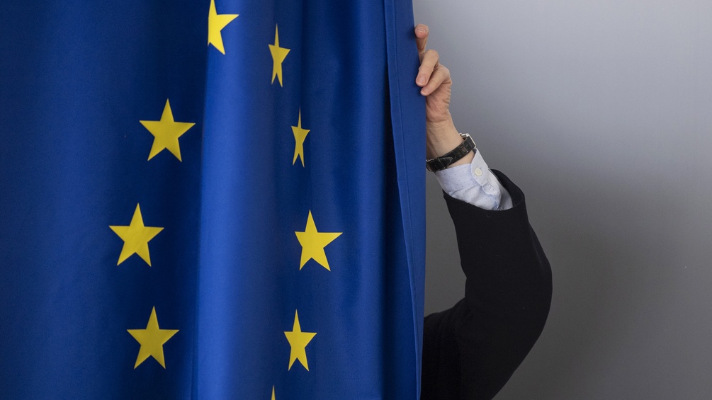Eine Frau zieht einen Vorhang zu, auf dem die Europa Flagge abgebildet ist