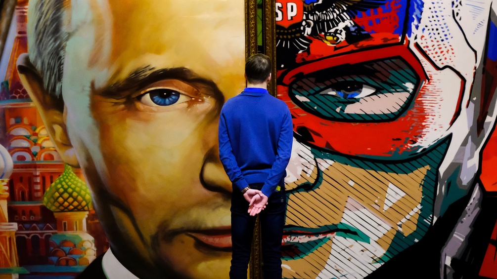 Ein junger Mann steht vor einem Gemälde von Putin.