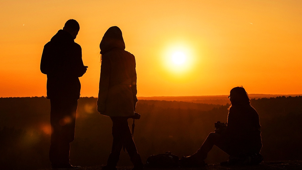 Ein Mann und zwei Frauen betrachten den Sonnenuntergang