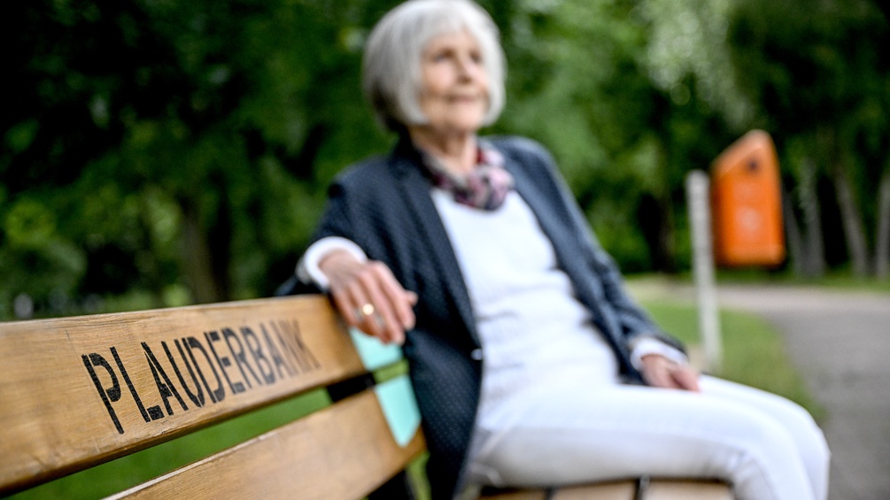 Eine ältere Frau sitzt auf der Plauderbank.