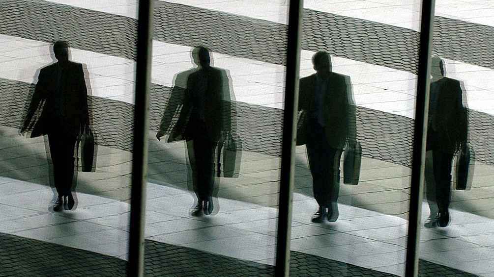 Ein Mann mit Aktentasche geht aus einem Bürogebäude. Er spiegelt sich in den Glasfenstern.