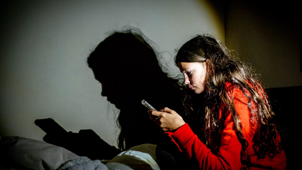 Mädchen sitzt und schaut auf ihr Handy