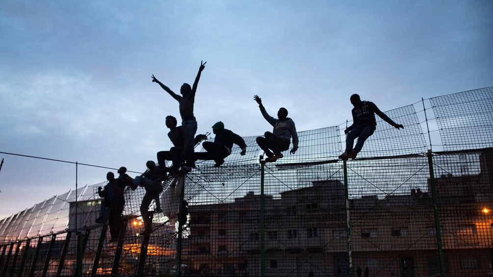 Menschen klettern über den Grenzzaun von Ceuta