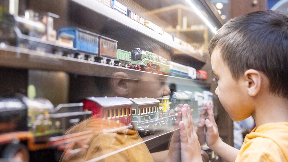 Kind im Spielzeugmuseum betrachtet Modelleisenbahnzüge
