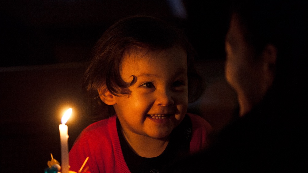 Ein Kind hält eine Kerze und lacht seine Mutter an.