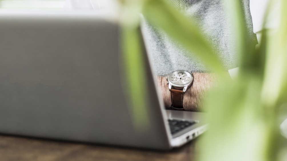 Älterer Herr mit Armbanduhr vor Laptop