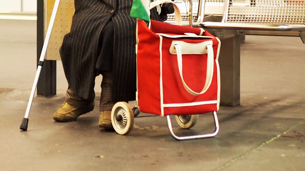 Alte Frau auf einer Bank mit Trolley