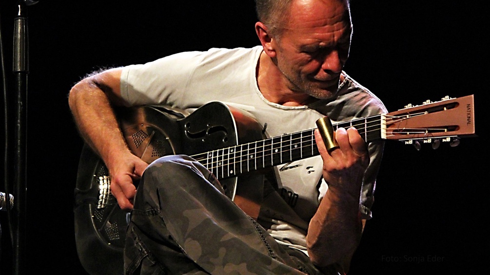 Peter Ratzenbeck sitzt auf der Bühne und spielt Gitarre.