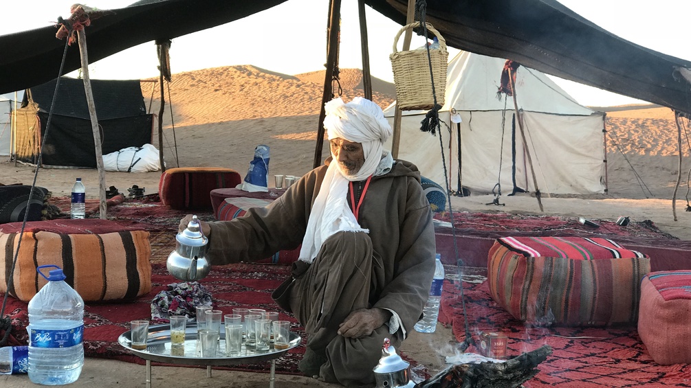 Mann gießt Tee ein in der Wüste, Zelt