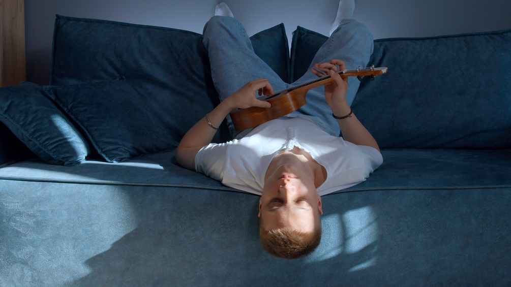 PICTUREDESK.COM/DPA PICTURE ALLIANCE/DANIL ROUDENKO Mann sitzt kopfüber mit Ukulele auf einem Sofa und hat die Augen geschlossen