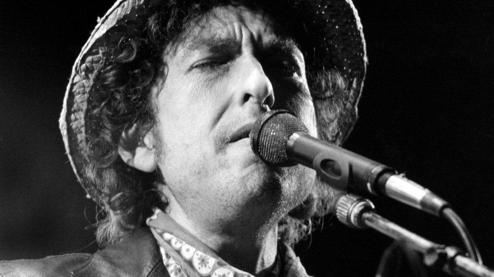 SW-Bild von Bob Dylan, singend mit Mikrophon.