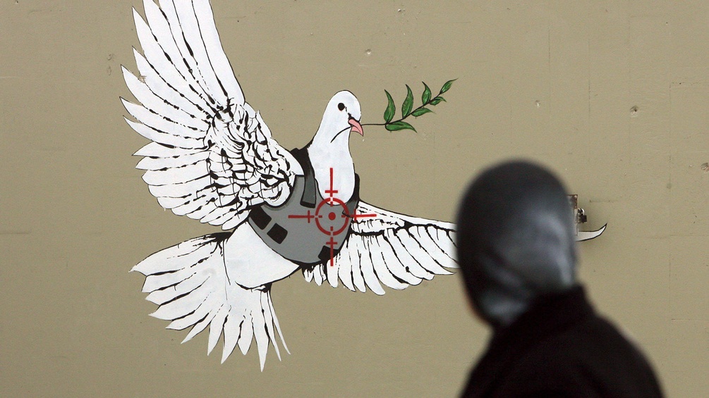 Graffiti vom Künstler Banksy von einer Friedenstaube mit schusssicherer Weste