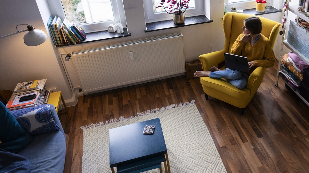 Person sitzt zuhause in einem gelben Armsessel und arbeitet am Laptop