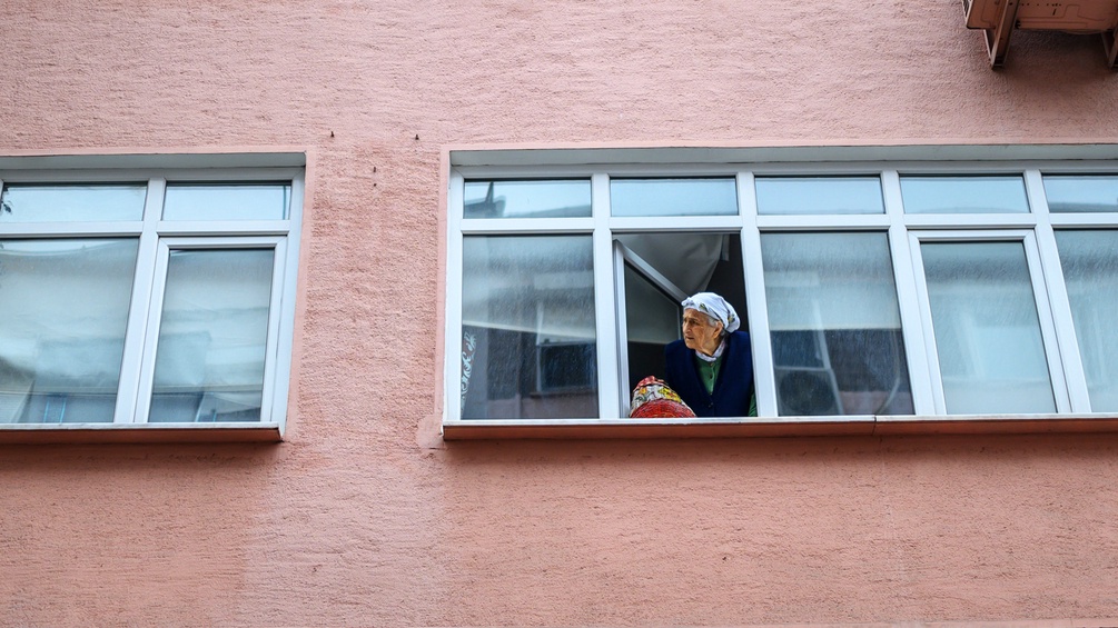 Eine ältere Frau sieht aus dem Fenster ihrer Wohnung.